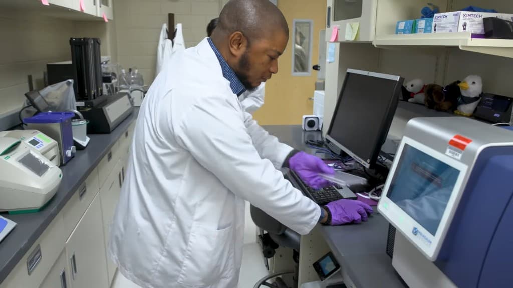 Scientist in a lab coat operating a microplate reader in the IDDD laboratory